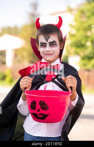 Gruseliger kleiner Junge im halloween Kostüm des Teufels mit Hörnern Haltekorb Stockfoto