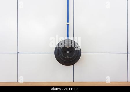 Alte schwarze elektrische EU-Steckdose auf einem Hintergrund Weiße Keramikfliesen Wand Stockfoto