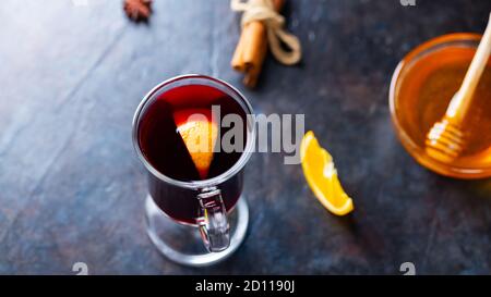 Weihnachtlicher Glühwein auf dunklem Hintergrund. Glühwein im Glas mit Zimt, Orangen und Honig. Heißer Weihnachtsdrink Stockfoto