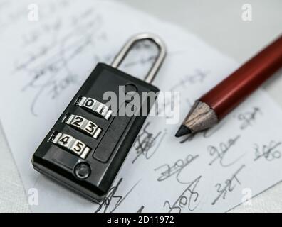 Auf ein Stück Papier werden dreistellige Codes geschrieben und dann mit dem Bleistift durchgestrichen. Ein dreistelliges Code-Vorhängeschloss. Stockfoto