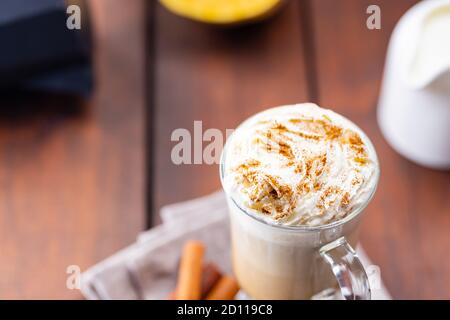 Kürbislatte, Milchkännchen und ein Stück Kürbis. Kürbislatte mit Schlagsahne und Gewürzen auf Holzbrettern. Heißer Herbstkaffee auf einem Laken-Nickerchen Stockfoto