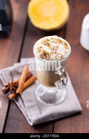 Kürbislatte, Milchkännchen und ein Stück Kürbis. Kürbislatte mit Schlagsahne und Gewürzen auf Holzbrettern. Heißer Herbstkaffee auf einem Laken-Nickerchen Stockfoto