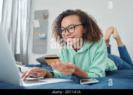 Fröhliche junge Mixed-Race-Hündin in Brillen und Casualwear online einkaufen Stockfoto