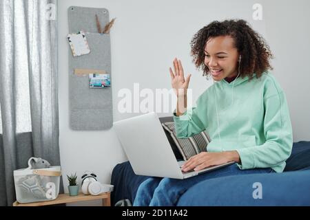 Junge fröhliche Mischrassenfrau winkt Hand zu ihrem Freund auf Notebook-Display Stockfoto