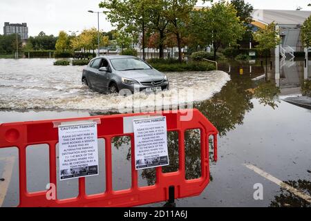 Aylesbury, Großbritannien. Oktober 2020. Sturm Alex Überschwemmungen in Aylesbury, Grafschaft Stadt Buckinghamshire. Ein Wochenende mit fast konstantem Starkregen veranlasste den Bear Brook, seine Ufer zu sprengen und den Vale Park und das Aqua Vale Swimming and Fitness Centre und seinen Parkplatz zu überfluten. Park Street Brücke neben dem überfluteten Vale Park zeigt Bear Brook Wassertiefe bis oben auf der Brücke. Das Auto erzeugt eine Flutwelle, als es den Parkplatz des Aqua Vale Swimming und Fitness Centers verließ. Die Schrankenwarnschilder wurden angebracht, wenn das Auto bereits geparkt war.Quelle: Stephen Bell/Alamy Stockfoto