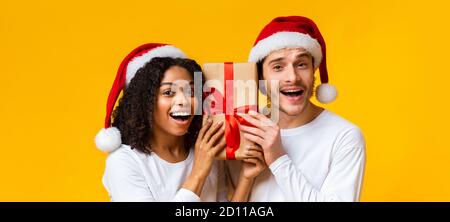 Aufgeregt interracial paar in santa Hüte halten Xmas Geschenkbox Stockfoto