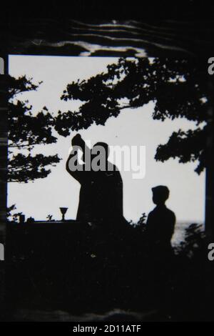 Schöne Vintage-Schwarz-Weiß-Fotografie eines römisch-katholischen Priesters aus den 1970er Jahren, der die heilige Messe mit der Eucharistie auf den offenen Feldern feiert. Stockfoto