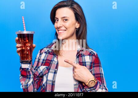 Junge schöne Frau trinkt Glas Cola Getränk lächelnd glücklich Zeigen mit Hand und Finger Stockfoto