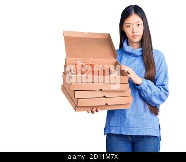 Junge schöne chinesische Frau hält Pappkartons der italienischen Pizza Denken Haltung und nüchternen Ausdruck selbstbewusst suchen Stockfoto