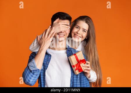 Mädchen schließt Augen zu Kerl und gibt ihm Geschenk Stockfoto