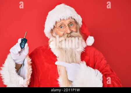 Alter älterer Mann mit grauen Haaren und langem Bart tragen santa claus Kostüm hält Auto Tasten lächelnd glücklich zeigen mit Hand und Finger Stockfoto