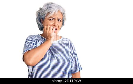 Ältere Frau mit grauen Haaren tragen lässige gestreifte Kleidung, die gestresst und nervös mit den Händen auf dem Mund beißen Nägel. Angstproblem. Stockfoto