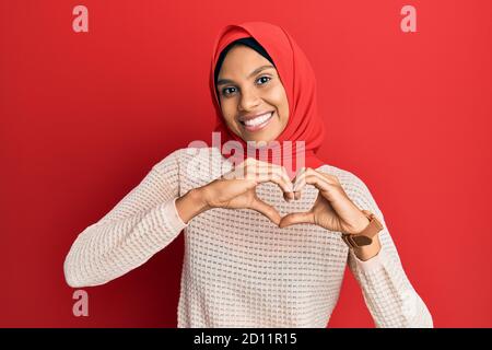 Junge afroamerikanische Frau trägt traditionelle islamische Hijab Schal lächelnd in der Liebe tun Herz Symbol Form mit Händen. Romantisches Konzept. Stockfoto
