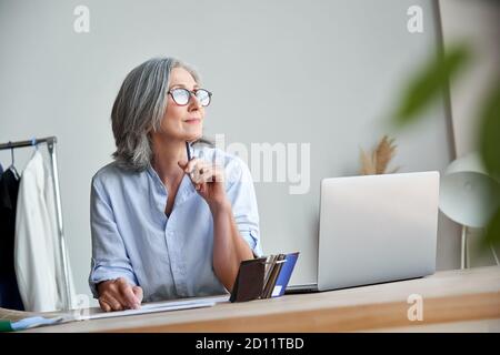 Inspirierte reife Frau Modedesignerin denken an neue kreative Ideen bei der Arbeit. Stockfoto