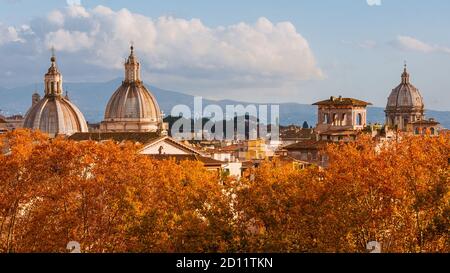 Skyline von Rom im Herbst. Barocke Kuppeln ragen über schöne rote und orangefarbene Blätter Stockfoto