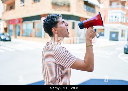 Junger hübscher kaukasischer Mann, der mit Megaphon in der Stadt schreit Stockfoto