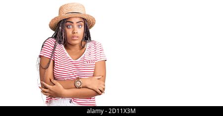 Junge afroamerikanische Frau mit Zöpfen tragen Sommerhut schütteln Und Frost für Winterkälte mit traurig und Schock Ausdruck Auf dem Gesicht Stockfoto