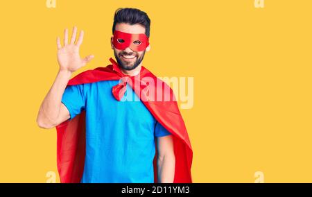 Junger schöner Mann mit Bart trägt Superhelden Kostüm zeigt und zeigt mit den Fingern Nummer fünf, während lächelnd zuversichtlich und glücklich. Stockfoto