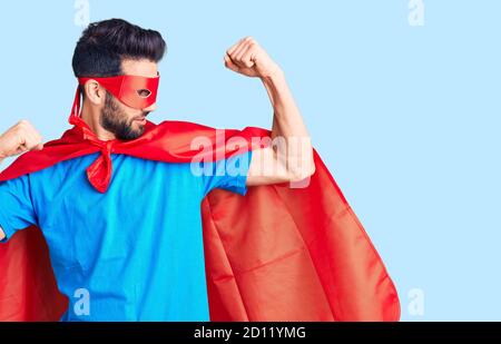 Junger schöner Mann mit Bart trägt Superhelden Kostüm zeigt Arme Muskeln lächelnd stolz. Fitness-Konzept. Stockfoto