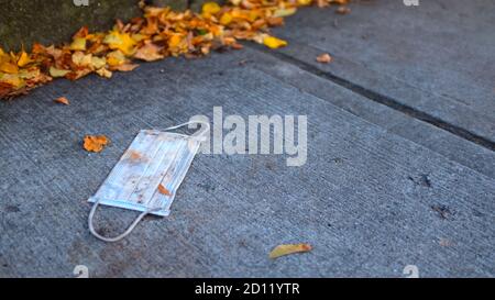 Blaue Einweg-Gesichtsmaske auf Gehsteig durch einen Stapel abgelegt Der Herbstblätter Stockfoto