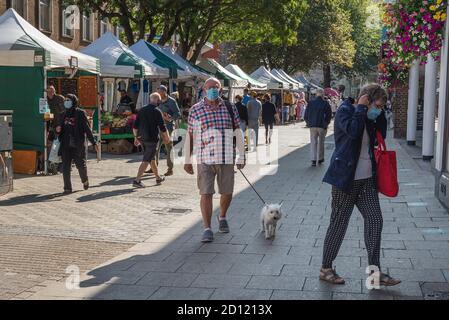 Mann mit Gesichtsmaske geht mit seinem Hund durch Canterbury High Street an einem sonnigen Tag. Stockfoto