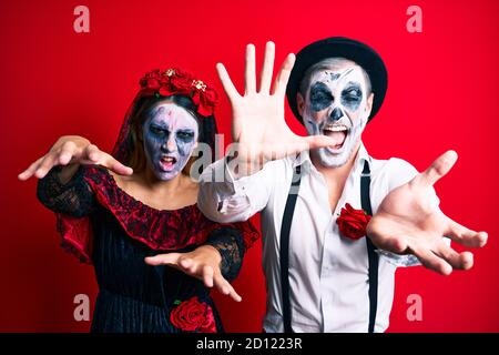 Schönes Paar trägt Tag der Toten Kostüm gestikuliert als Zombie über isolierten roten Hintergrund. Stockfoto