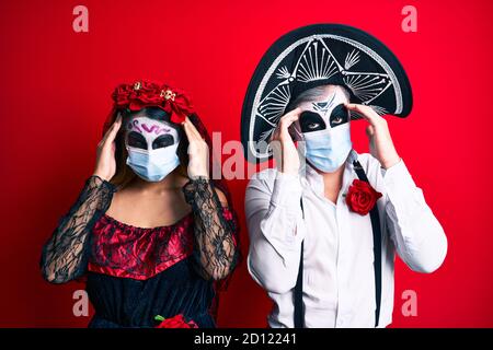 Paar trägt Tag des Toten Kostüm trägt medizinische Maske leiden unter Kopfschmerzen verzweifelt und gestresst, weil Schmerzen und Migräne. Hände auf dem Kopf. Stockfoto