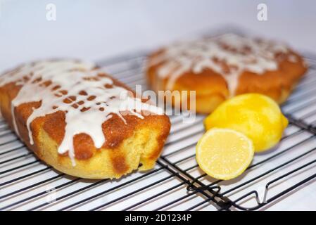 Zwei ganze hausgemachte Zitrone Nieselkuchen auf einem Draht Kuchen Kühlgestell. Stockfoto