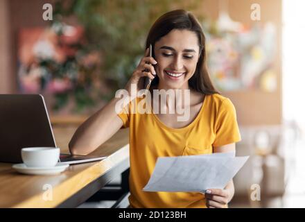 Glückliche arabische Dame mit Gespräch am Telefon, halten Dokumente Stockfoto