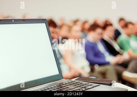Laptop auf Business-Präsentationstisch mit verblurten Menschen im Hintergrund Bokeh. Stockfoto