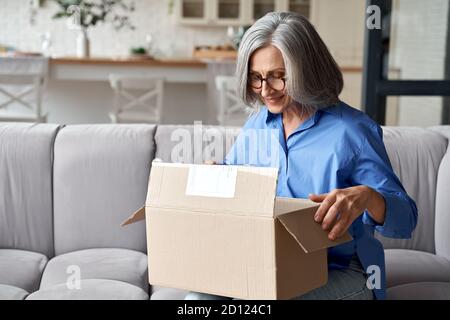 Lächelnd ältere Frau Auspacken Paket Postkasten zu Hause auf Couch. Stockfoto