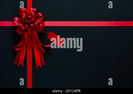 Rotes Band mit Schleife und Preisschild auf schwarzem Hintergrund. Black friday Konzept. Stockfoto