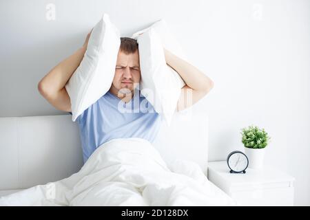 Derpression, Schlaflosigkeit und Kopfschmerzen Konzept - Porträt von müde jungen Mann auf dem Bett sitzen und hält Kissen auf dem Kopf Stockfoto