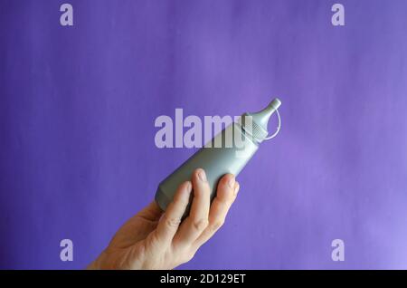 Männliche Hand und graue Plastikflasche mit Sirup. Der Mann hält eine neue Flasche Süßsirup für Eis und Desserts. Selektiver Fokus. Stockfoto