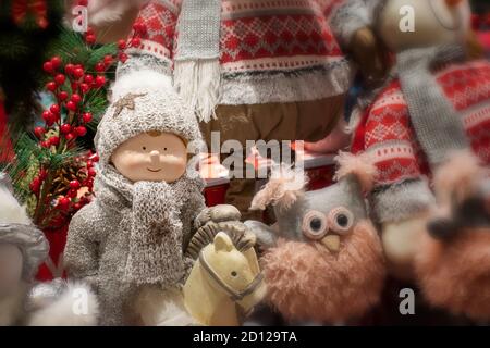 Niedliche Babypuppe im Winterkostüm auf einem Pferd, Strickmütze und Schal. Lag flauschige Eule und andere Weihnachtsspielzeug Geschenke. Verwackelte Hintergrundkulisse Stockfoto