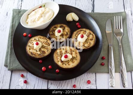 Gebratene Aubergine gefüllt mit Knoblauchsauce und Preiselbeeren, garniert mit Basilikumblättern auf einem dunklen Teller auf Holzhintergrund. Draufsicht. Stockfoto