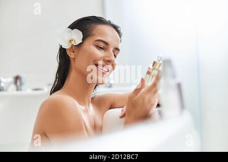 Fröhliche junge Frau hält Vitamin-Serum während des Bades Stockfoto