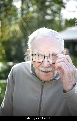 Fröhlicher grauhaariger alter Mann schaut auf den Gesprächspartner und lächelt. Der alte Mann kann ohne Brille nicht sehr gut sehen. Porträt eines fröhlichen alten Mannes Stockfoto