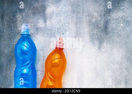 Blaues und orangefarbenes isotonisches Energiegetränk auf grau-blauem Hintergrund. Sportkonzept. Draufsicht, Kopierbereich für Text, selektiver Fokus Stockfoto