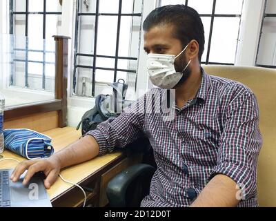 Ein maskierter Mann aus Asien arbeitet im Büro nach der Sperre des Coronavirus. Stockfoto