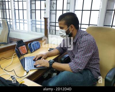 Ein maskierter Mann aus Asien arbeitet im Büro nach der Sperre des Coronavirus. Stockfoto