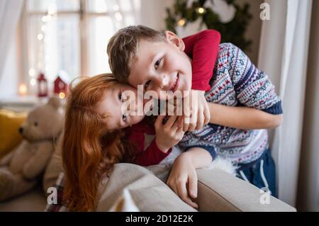 Kleine Mädchen und Jungen drinnen zu Hause zu Weihnachten, Blick auf die Kamera. Stockfoto