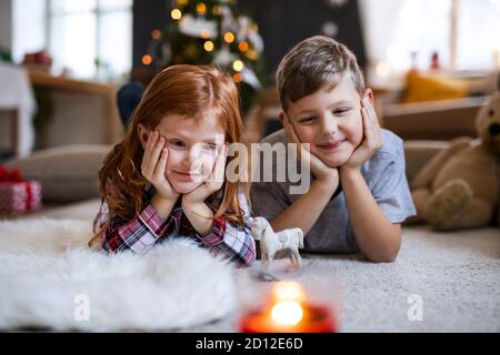 Kleines Mädchen und Junge drinnen zu Weihnachten zu Hause, auf dem Boden liegend. Stockfoto