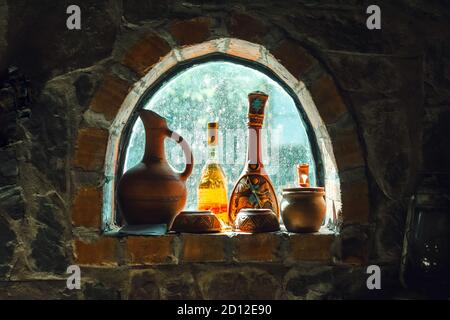 Alte rustikale Weinflaschen, Krüge auf einem kleinen Kellerfenster an einer Steinmauer Stockfoto