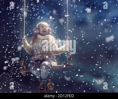 Glückliches Kind Mädchen spielt auf einem verschneiten Winterspaziergang. Kleines Mädchen genießt das Spiel. Kind Mädchen spielen auf Schaukel im Freien im Schnee. Outdoor-Spaß für Winter vac Stockfoto