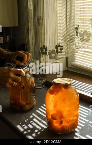 Eine Frau rollt ein Kompott in einem großen Glas unter Die Sonne im Sommer zu Hause im Dorf Stockfoto