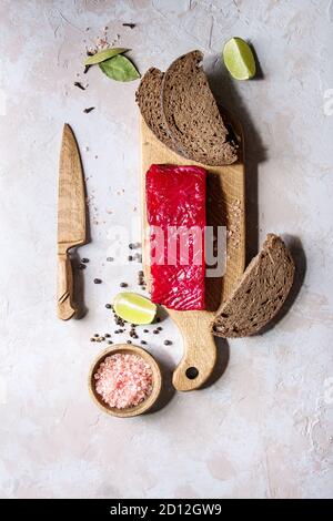 Stück rote Bete mariniertes gesalzenen Lachs mit in Scheiben geschnittenen Roggenbrot, rosa Salz, Pfeffer und Kalk auf Holz Schneidebrett serviert über grau Textur backgroun Stockfoto