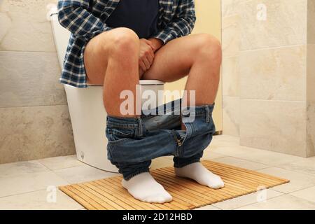 Ein Mann sitzt mit der Hose auf der Toilette Stockfoto