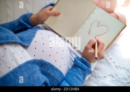 Draufsicht auf unkenntlich schwangere Frau drinnen zu Hause, Zeichnung Herzform. Stockfoto