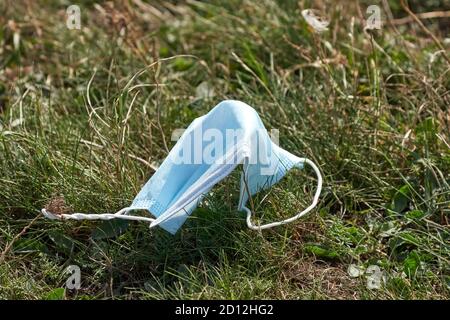 Gebrauchte Medizinische Gesichtsmaske auf dem Boden im Gras. Entsorgen Sie die gebrauchte Gesichtsmaske nicht ordnungsgemäß. Umweltverschmutzung während der Pandemie von Covid-19 Stockfoto